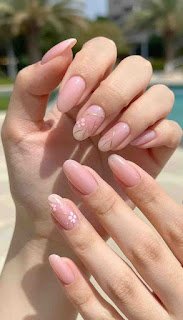 A close-up shot of beautifully manicured hands showcasing a stunning summer 2026 nail art trend. The nails are painted in a soft, luxurious pink acrylic finish, with subtle, delicate nail art designs that include thin gold lines and tiny floral accents. A gently blurred background features a sunlit outdoor setting, enhancing a warm and inviting atmosphere. The hands are elegantly posed on a light-colored surface, with soft, diffused natural lighting illuminating the nails, emphasizing their glossy finish. The overall mood is fresh and chic, perfect for summer, reflecting modern elegance and sophistication in nail art. beautifully manicured hands showcasing a stunning summer 2026 nail art trend