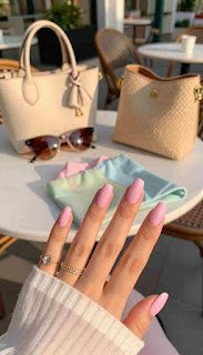 A close-up of elegantly manicured hands showcasing summer 2026 nail color trends, specifically a soft pink acrylic nail design with a glossy finish. The foreground features well-groomed fingers gently holding a stylish summer accessory, like a pair of sunglasses or a trendy tote bag. In the middle, a pastel-colored summer outfit drapes on a nearby table, complementing the pink nails. The background features a vibrant outdoor café scene bathed in warm, golden sunlight, accentuating the relaxed summer atmosphere. The composition captures soft shadows and a bokeh effect behind the accessories, creating a chic and inviting mood. This scene highlights the harmony between chic summer fashion and fresh, modern nail art. elegantly manicured hands showcasing summer 2026 nail color trends