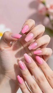 A close-up of perfectly manicured pink acrylic nails on a stylish hand, displaying a smooth and glossy finish. The nails are various shades of light to vibrant pink, showcasing intricate details like subtle glitter and ombre effects. The hand is elegantly poised against a soft, pastel-colored background, featuring hints of summer florals, creating a warm and inviting atmosphere. Soft, natural daylight filters in, casting delicate shadows that highlight the shine of the nails. The focus is sharp on the nails themselves, while the background is slightly blurred, enhancing the subject’s prominence. The overall mood is fresh, trendy, and perfectly capturing the essence of the summer nail color trend for 2026. perfectly manicured pink acrylic nails on a stylish hand